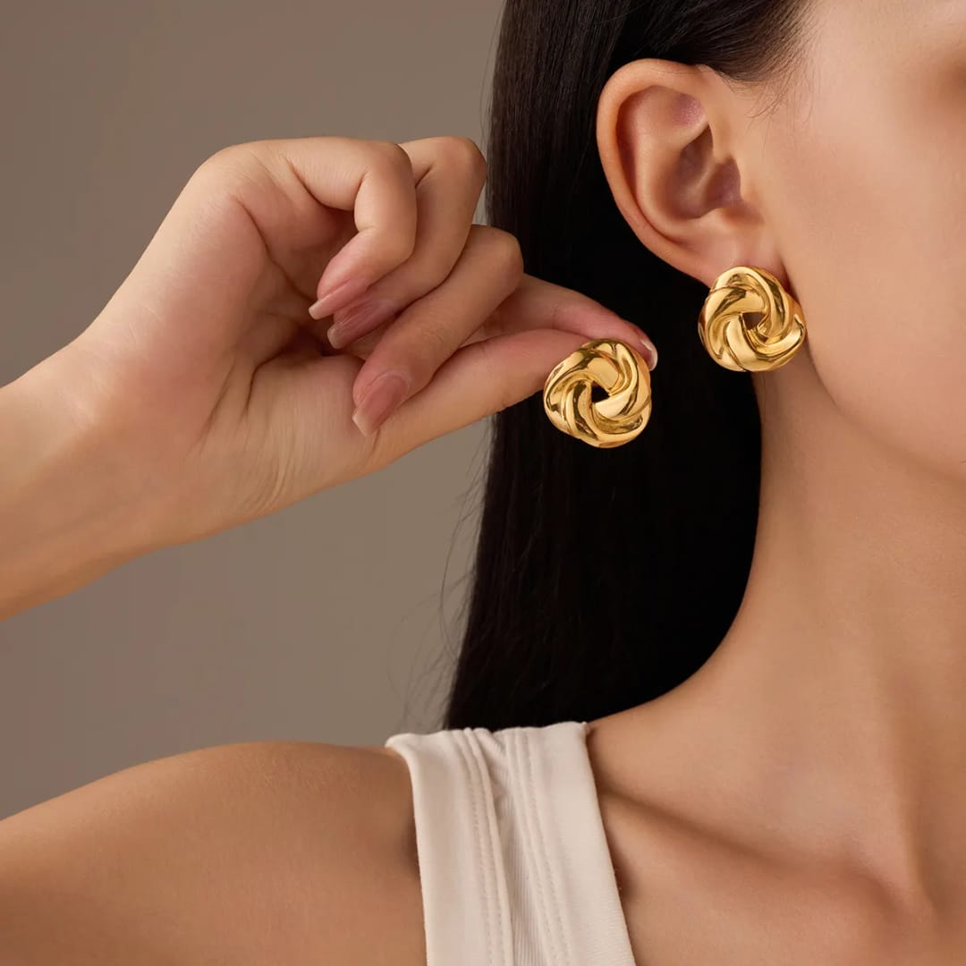 Gold earrings being worn by a person against a neutral background