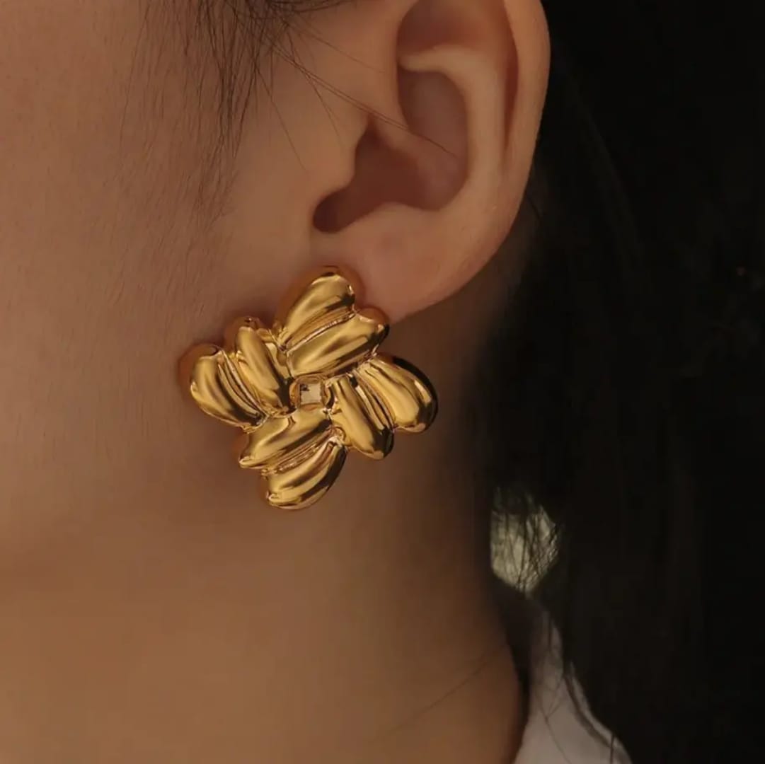 Gold floral earring worn on an ear with a blurred background