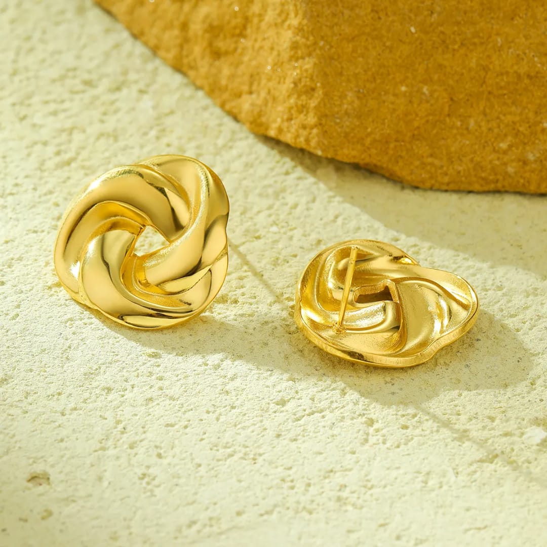 Pair of gold knot earrings on a textured beige surface