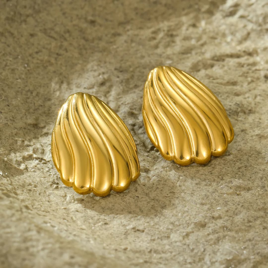 Gold shell-shaped earrings on a textured beige surface